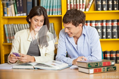 Image of Students Studying At Table Against Bookshelf In Library