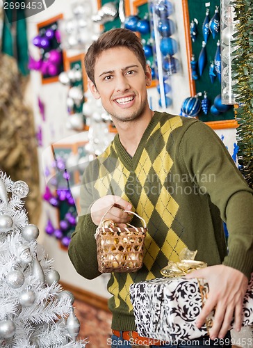 Image of Man Holding Christmas Present And Bauble Basket In Store