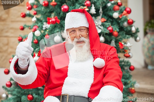 Image of Santa Claus Gesturing Thumbsup Against Christmas Tree