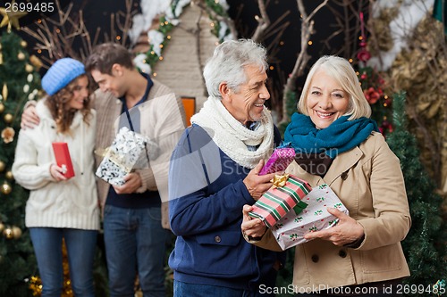 Image of Senior Couple Holding Christmas Presents With Children In Backgr