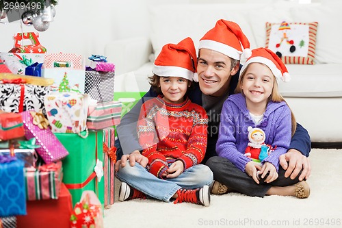 Image of Father And Siblings Sitting By Stacked Christmas Presents