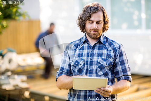 Image of Carpenter Using Digital Tablet With Coworker Working In Backgrou