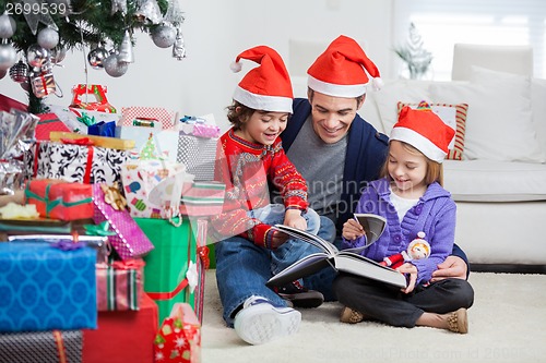 Image of Siblings And Father Reading Book By Christmas Presents