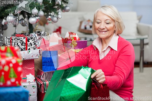 Image of Woman Looking In Bag While Sitting By Christmas Gifts