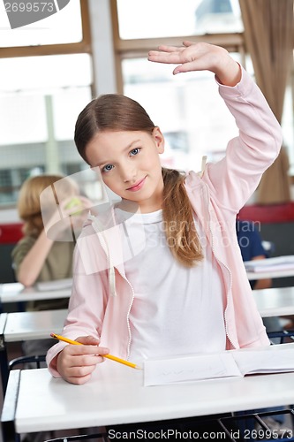 Image of Schoolgirl Raising Hand At Desk In Classroom