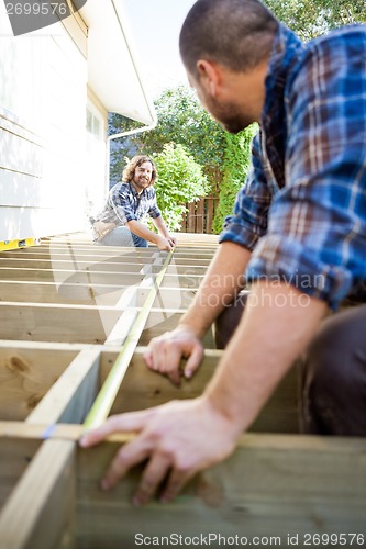 Image of Carpenter Measuring Wood With Tape While Looking At Coworker