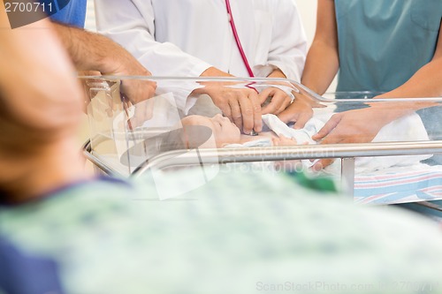 Image of Doctor Examining Baby While Standing By Nurse