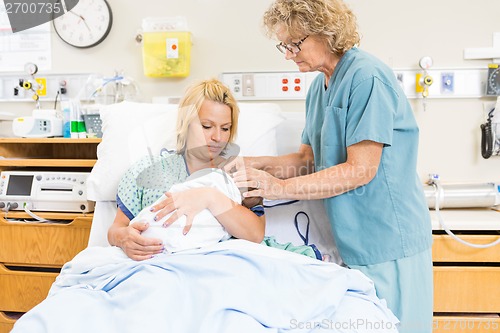 Image of Female Nurse Assisting Woman In Breast Feeding Baby In Hospital