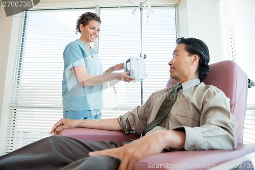 Image of Nurse Looking At Patient While Adjusting IV Machine