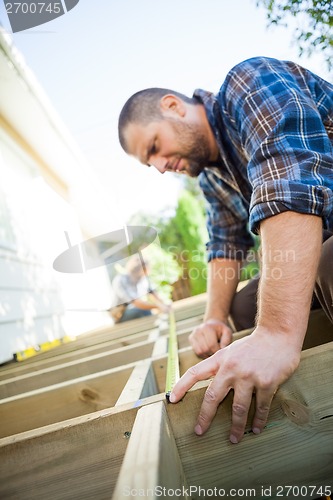 Image of Carpenter Measuring Wood With Tape While Coworker Assisting Him