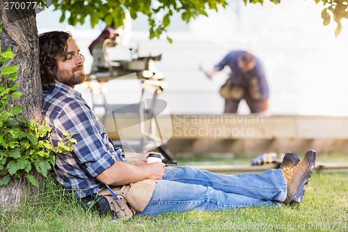 Image of Relaxed Carpenter Holding Disposable Cup While Leaning On Tree T