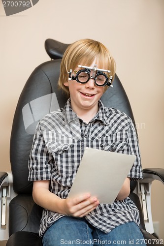 Image of Boy With Trial Frame Reading Test Chart On Chair