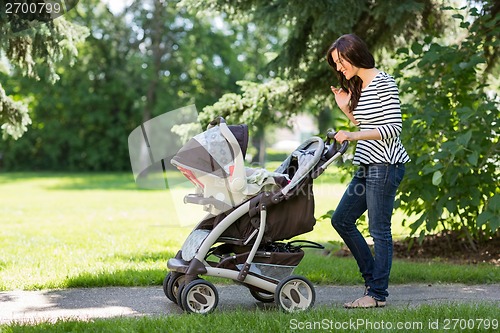 Image of Woman Looking Into Baby Carriage In Park