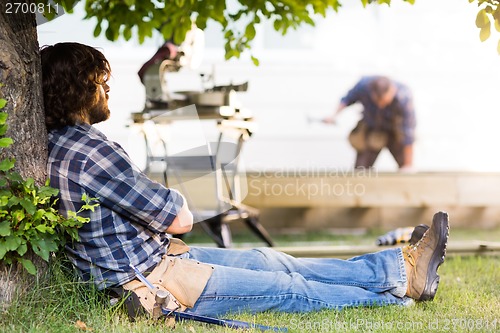 Image of Construction Worker Leaning On Tree Trunk