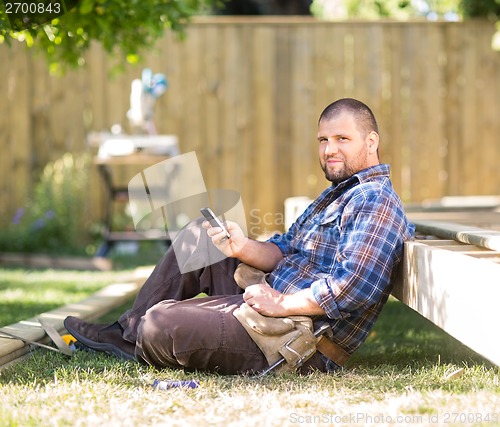 Image of Confident Carpenter Messaging On Cellphone While Leaning On Wood