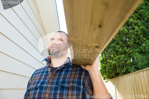 Image of Carpenter Carrying Plank On Shoulder At Construction Site