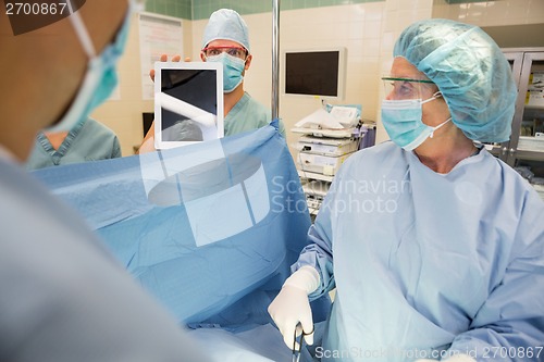 Image of Nurse Showing Digital Tablet To Surgeons During Surgery