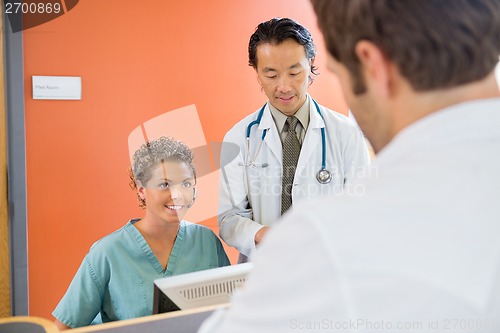 Image of Nurse Looking At Patient With Doctor Standing By In Hospital