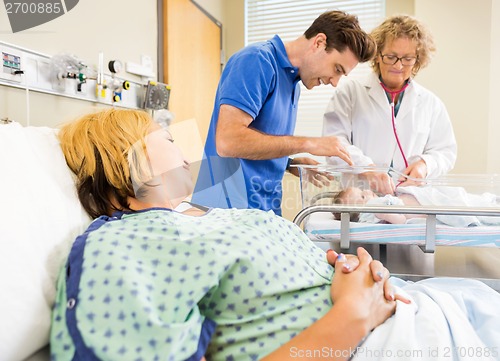 Image of Mature Doctor Examining Newborn Babygirl While Parents Looking A