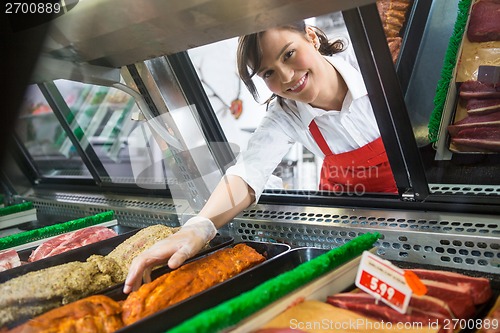 Image of Saleswoman Picking Meat Displayed In Cabinet