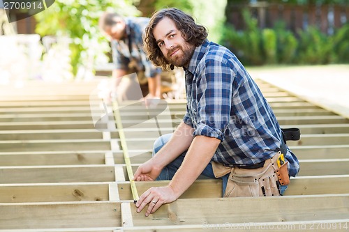 Image of Carpenter Measuring Wood With Tape While Coworker Assisting Him