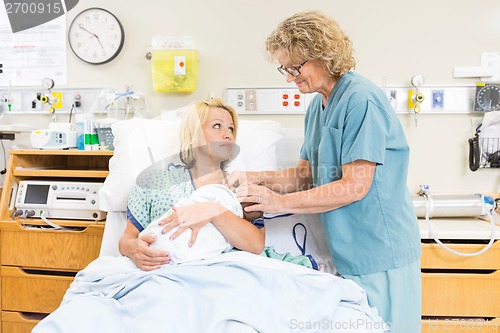 Image of Smiling Nurse Assisting Woman In Breast Feeding Baby In Hospital