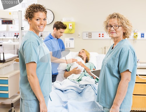 Image of Smiling Nurses Standing Against Couple With Baby In Background