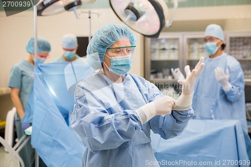 Image of Doctor Wearing Surgical Gloves With Team In Background