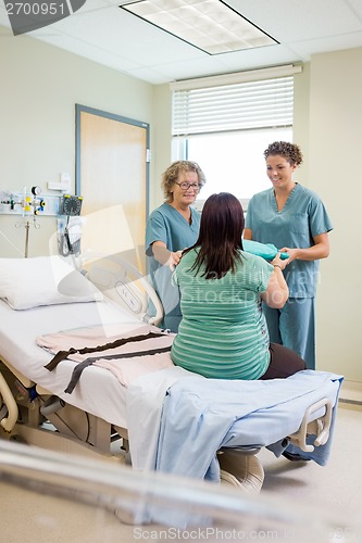 Image of Nurse Giving Gown To Pregnant Woman While Colleague Standing By
