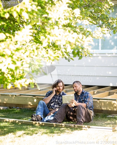 Image of Worker Showing Digital Tablet To Coworker On Call At Site