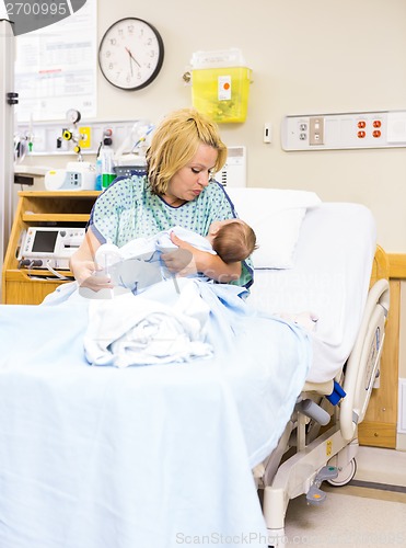 Image of Mother Looking At Newborn Baby While Sitting In Hospital Bed