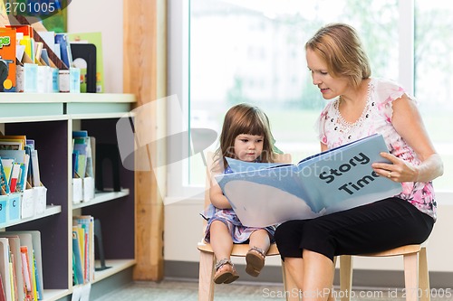 Image of Teacher With Cute Girl Reading Book In Library
