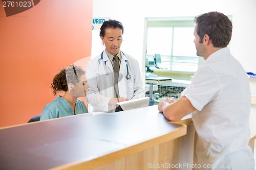 Image of Medical Team Using Digital Tablet While Patient Standing At Rece