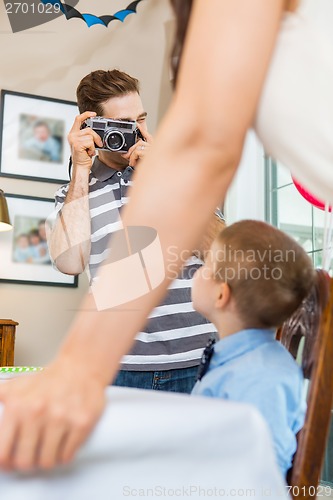 Image of Man Taking Picture Of Family At Birthday Party