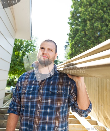 Image of Carpenter Carrying Planks On Shoulder At Construction Site