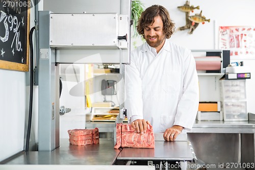 Image of Smiling Butcher Slicing Meat In Machine