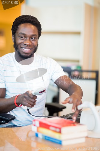 Image of Smiling Librarian Scanning Books At Library Desk