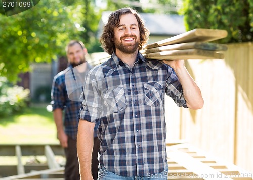 Image of Carpenter With Coworker Carrying Planks Outdoors