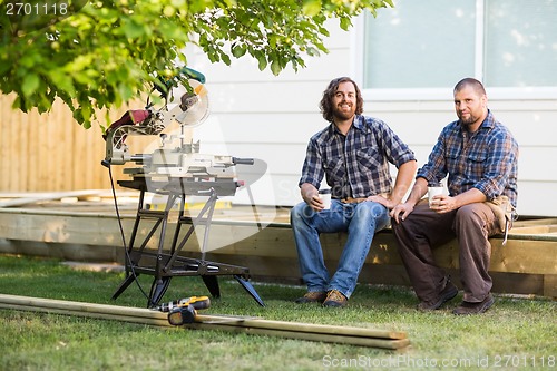 Image of Carpenters Holding Disposable Cups While Sitting On Wooden Frame