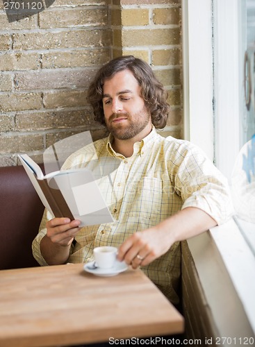 Image of Man With Coffee Cup Reading Book In Cafe