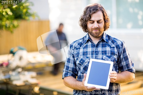 Image of Carpenter Displaying Digital Tablet With Coworker Working In Bac