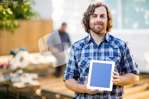 Image of Carpenter Displaying Tablet Computer With Coworker Working In Ba