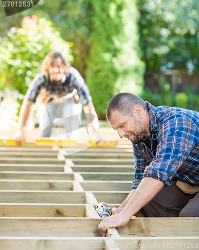 Image of Carpenter Drilling Wood With Coworker In Background