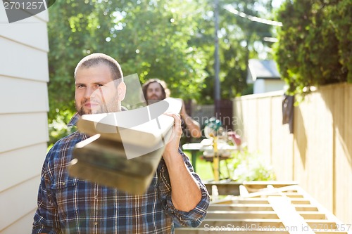 Image of Male Carpenter And Coworker Carrying Lumbers At Construction Sit