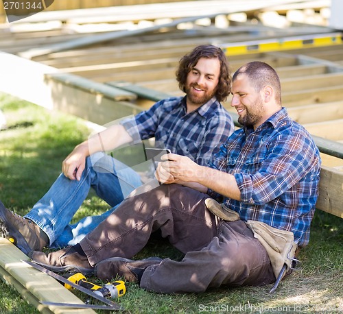 Image of Happy Carpenters Looking At Mobile Phone At Construction Site