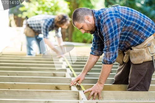 Image of Carpenters Measuring Wood With Tape At Construction Site