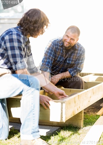 Image of Worker Looking At Coworker Measuring Wood At Site