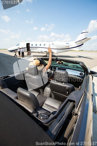 Image of Woman In Convertible Waving To Pilot And Stewardess Against Jet