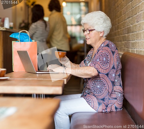 Image of Senior Woman Using Laptop While Having Coffee In Cafeteria