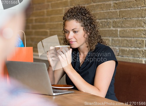 Image of Woman Looking At Laptop While Drinking Coffee At Cafe Table